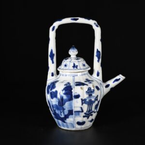 Photo d'une théière en porcelaine d'époque Kangxi à décor bleu et blanc de paysages et d'objets précieux, elle a la particularité d'avoir une anse supérieure.