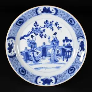 Photo d'une assiette en porcelaine d'époque Kangxi, à décor bleu et blanc de personnages sur un balcon.