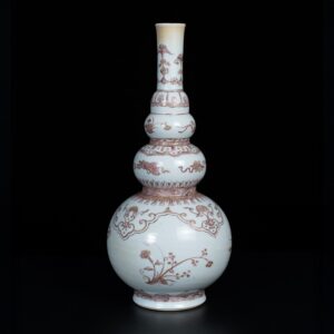 Photo d'un vase en porcelaine d'époque Kangxi, de forme triple gourde, il est décoré en rouge-de-fer de rinceaux fleuris et objets précieux.
