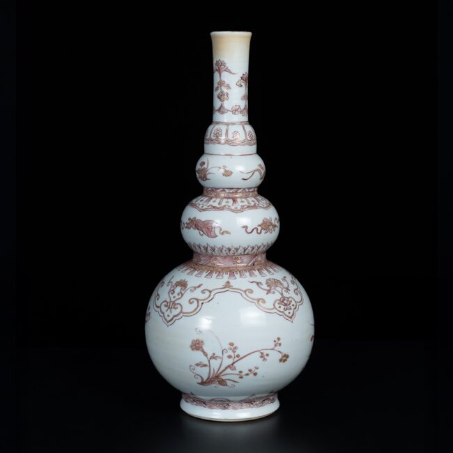 Photo d'un vase en porcelaine d'époque Kangxi, de forme triple gourde, il est décoré en rouge-de-fer de rinceaux fleuris et objets précieux.