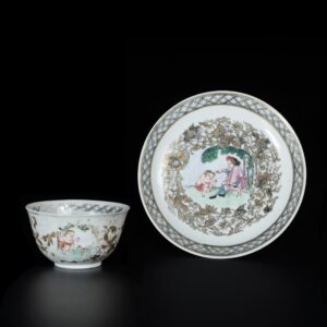Photo d'une tasse et sa soucoupe en porcelaine coquille d’oeuf, d'époque Qianlong, aux émaux de la Famille Rose à décor d’un hollandais fumant la pipe et d’un homme à moitié nu accroupi.
