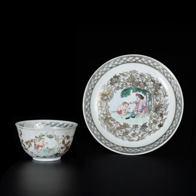 Photo d'une tasse et sa soucoupe en porcelaine coquille d’oeuf, d'époque Qianlong, aux émaux de la Famille Rose à décor d’un hollandais fumant la pipe et d’un homme à moitié nu accroupi.